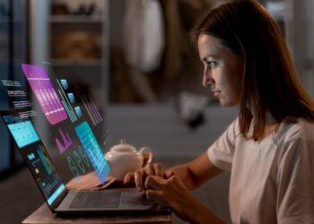 Mulher trabalhando em laptop com gráficos holográficos de dados e IA, demonstrando como usar a IA para ganhar dinheiro através de análise digital