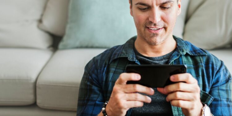 Melhor Celular para Jogar: Testei 20 e Estes 5 São Incríveis 1 Homem jogando no melhor celular para jogar sentado no sofá segurando smartphone com as duas mãos