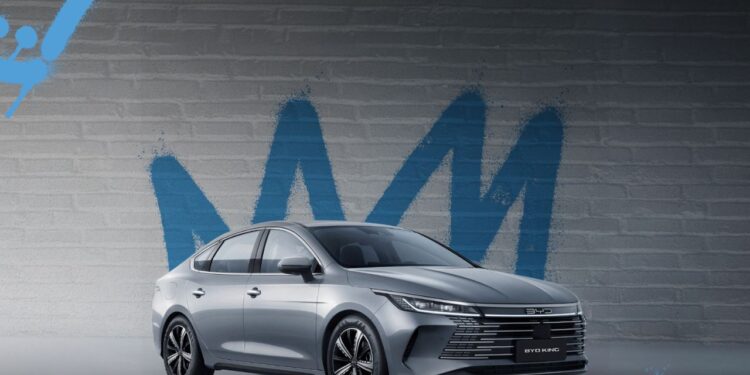 BYD King L: O Híbrido de R$ 199 Mil Que Faz 2.100 km Sem Parar 1 BYD King L sedã híbrido prata estacionado em frente a parede com grafite azul, mostrando design moderno e elegante do veículo chinês