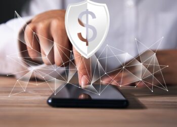 Como Cancelar o Seguro Prestamista: O Guia Definitivo Para Se Livrar da 'Venda Casada' e Recuperar Seu Dinheiro 3 Mão toca smartphone com ícone de escudo e cifrão, representando o direito de cancelar seguro prestamista.